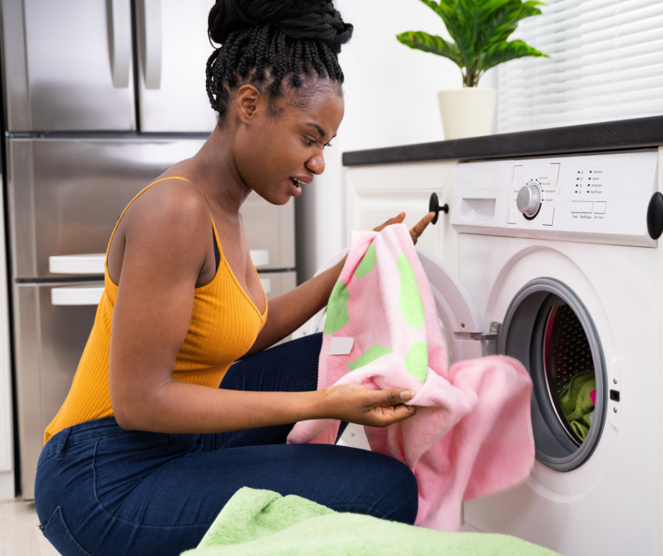black woman is pulling a shirt from a washer with a disgusted look on her face looking at a stain on the shirt