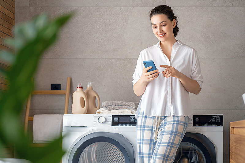 woman looking at phone leaning against washing machine